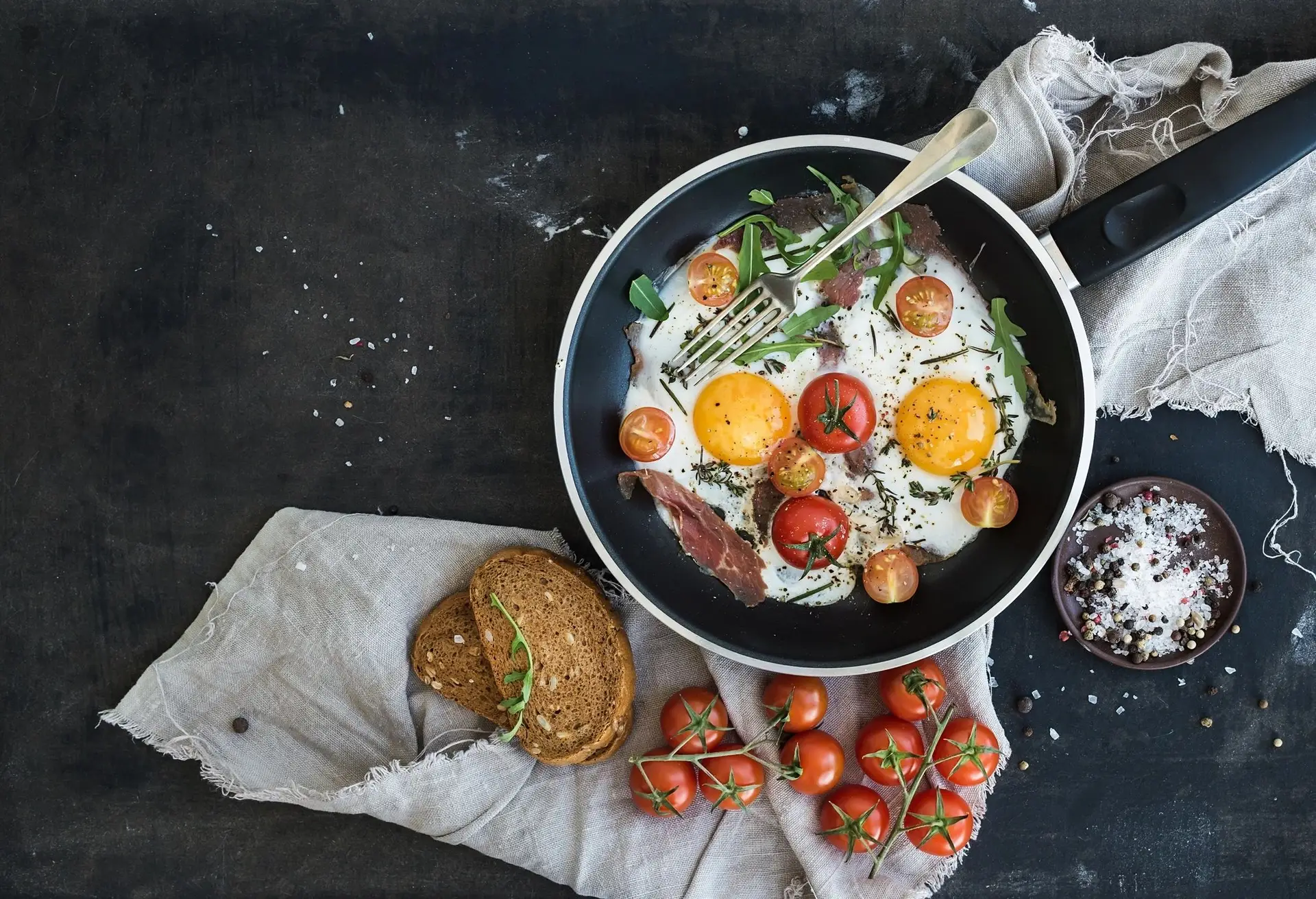 breakfast being cooked in a frying pan with sourdough toast, cherry tomatoes and fresh ingredients